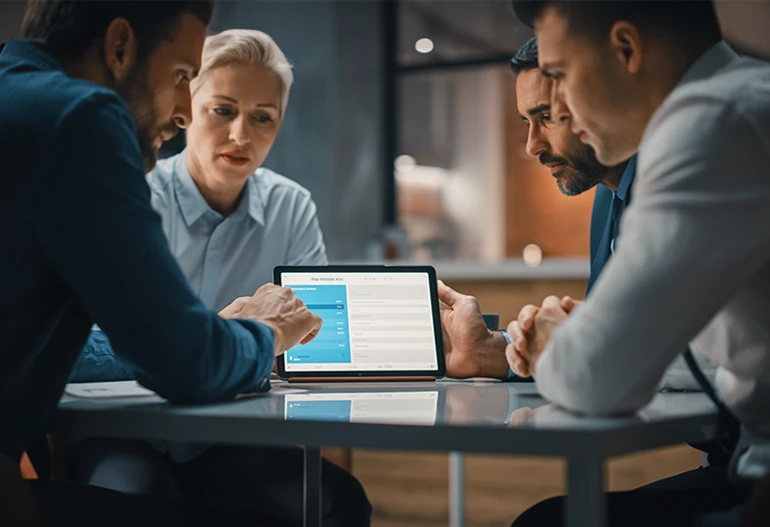 Symbolbild: Vier Personen sitzen am Tisch und analysieren gemeinsam Daten auf einem Laptop – Beratung für Dokumenten- & Drucklandschaften